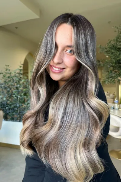 Cheveux longs ondulés avec balayage blond cendré et racines foncées, coiffure lumineuse en salon