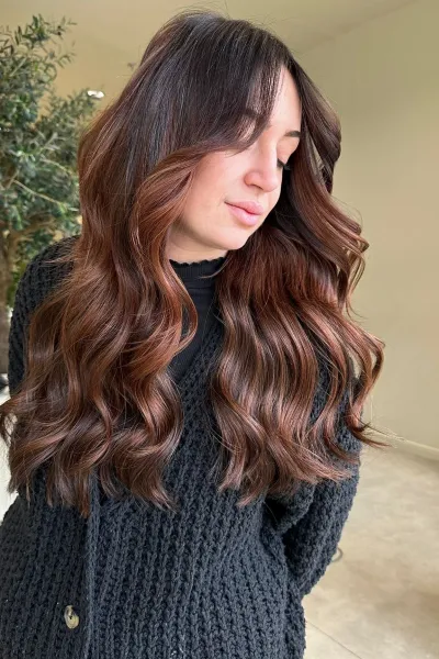 Cheveux longs ondulés avec coloration brun cuivré, reflets chauds et finition naturelle
